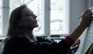 Cate Blanchett as Lydia Tar in the film TAR, sitting at her piano and writing notes on a musical score.