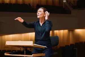 Cate Blanchett as Lydia Tar in TAR, standing in a concert hall at the conductor's podium.