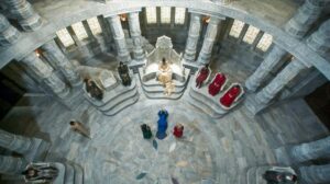 The Hall of Sitters in the White Tower, viewed from high above. White stone seats on low stone plinths form a ring around the edge of the Hall, and seated here are groups of Aes Sedai belonging to the seven color-coded Ajahs, though only the Green and Red Sitters are visible. Between these two groups is a large throne, and here is seated the Amyrlin Seat. Before her stand two women, while a third, wearing blue, kneels on the ground.