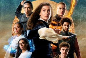 Official poster for The Wheel Of Time season two. In the center stands Moiraine, wearing a dark blue vest over a white blouse with a long blue dress. She holds a short knife. Her brown hair is unbound. To the right of her are Rand, with a shaven head, coiled in orange threads of the One Power; Perrin, wearing a dark green woven leather vest over a red shirt; and Mat, wearing a dirty olive-green coat with unkempt curly hair. To the left of her are Lan, reaching over his shoulder for the sword strapped to his back; Nynaeve, wearing white and staring defiantly at the camera; and Egwene, wearing white, with blue threads of the One Power winding around her. They are all superimposed against a large gold disc on a blue background.