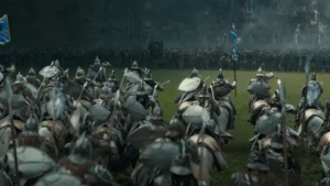 A line of Elves on horseback gallops across a grassy field to meet an army of orcs, who have with them a tall cage containing the small figure of a person. The Elves carry spears and swords, and wear silver armor. Their banners are blue.