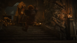 Owain Arthur as Durin IV, flying backwards down a short flight of steps leading up to a dais where Peter Mullan as Durin III stands, hand upraised. Durin IV has red hair and wears red armor over a red-and-gold tunic. Durin III has long white hair and wears a dark robe.