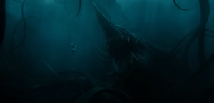 Underwater wide shot of a woman in a white dress sinking, while an enormous sea-monster rises out of the ocean depths to face her. The creature has the snout of a goblin shark, the mouth of a lamprey, and numerous tentacles like a squid's.