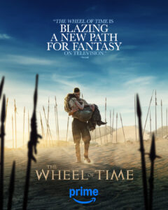 First poster for The Wheel of Time season three, depicting Josha Stradowski as Rand al'Thor walking through a desert between rows of standing spears that cast long shadows in the early morning light. He is carrying Rosamund Pike as Moiraine Damodred in his arms. Rand has short reddish-brown hair and wears a short-sleeved sand-brown shirt with brown trousers. He has dragon tattoos spiraling down his bare forearms. Moiraine, whose face is turned away from the camera, has long brown hair and wears a sand-brown blouse and a gray dress.