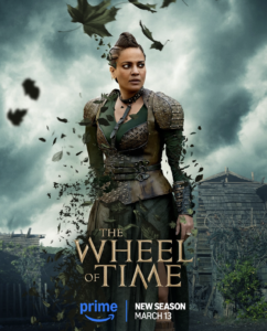 Poster of Priyanka Bose as Alanna Mosvani. She has dark hair pulled back in braids. She wears brown leather armor with a collar over a dark green dress with thigh-high slits. Her body and clothes are dissolving into leaves. Text reads “The Wheel Of Time: New Season, March 13th”.